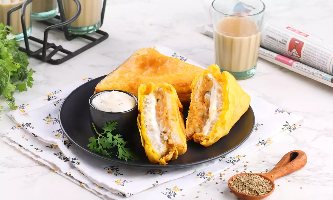 Golden triangular bread pakoras with a crisp texture, stuffed with creamy white mayo filling, served on a black plate with chutney and parsley