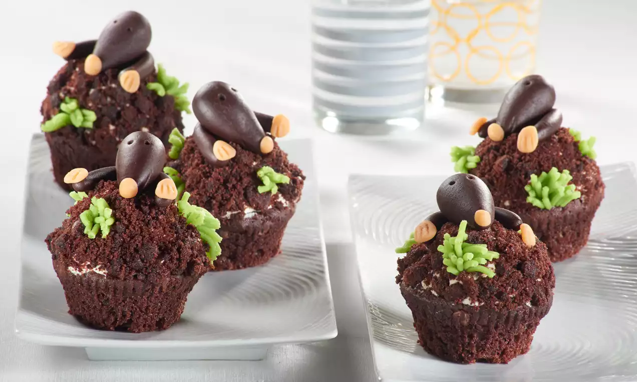 Schokoladenmuffins mit dunkler Streuselkruste, dekoriert mit Maulwürfen aus Schokolade und grünem Zuckerguss auf weißen Tellern