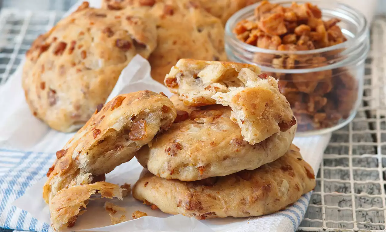 Škvarkové placky zlatavé a mírně nadýchané, s nepravidelným zakulaceným tvarem, na podložce vedle sklenice plné drobných škvarků