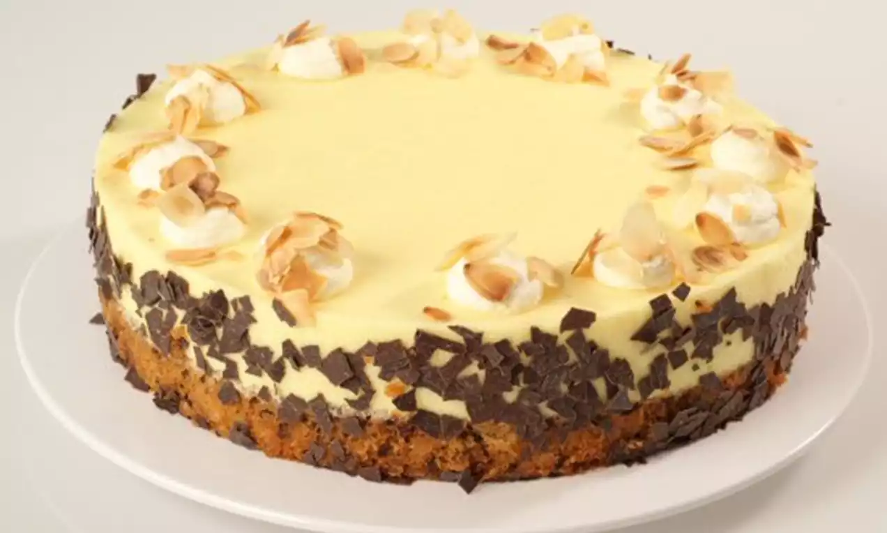 Weinsahnetorte mit hellgelber Creme, gerösteten Mandelblättchen und Sahnetupfen, auf braunem Boden mit Schokoladenstückchen verziert