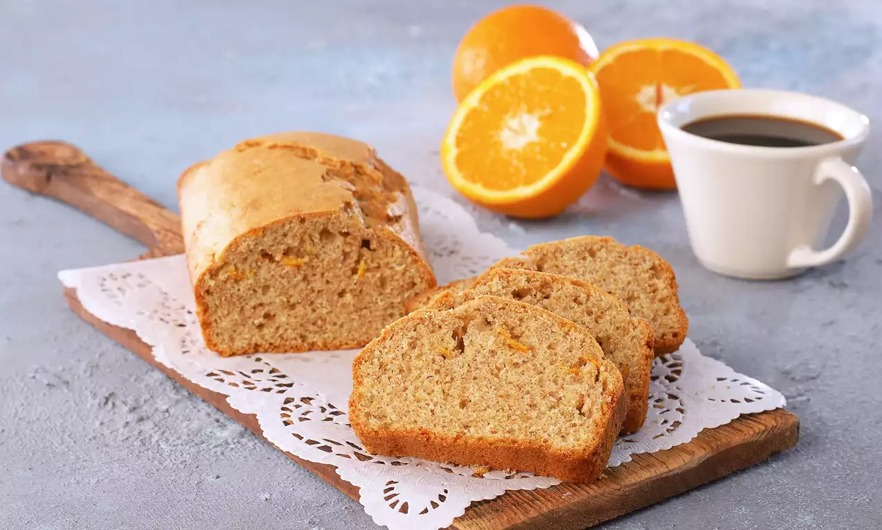 Tam buğday unlu portakallı kek dilimleri doğal dokulu, turuncu benekli, ahşap servis tahtasında dantel örtüyle sunulmuş