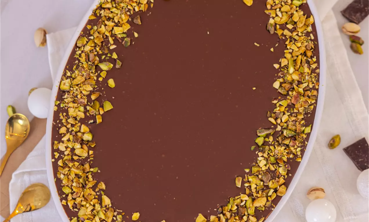 Dubai čokoladni tiramisu u ovalnom bijelom tanjuru, tamnosmeđi sjajni sloj prekriven usitnjenim zelenkastim pistacijama uz rub