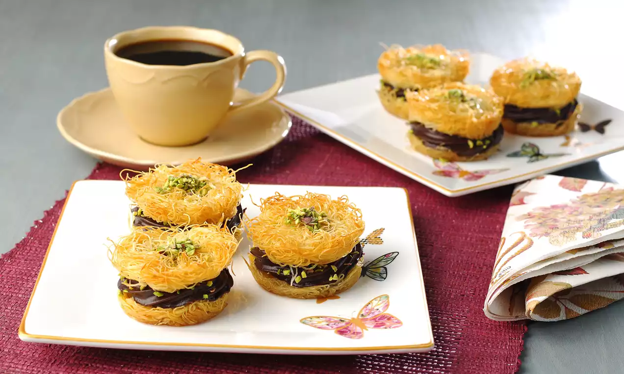 Altın rengi çıtır kadayıf katmanları arasında yoğun çikolatalı supangle dolgusu, üzerine ince kıyılmış yeşil fıstık serpilmiş