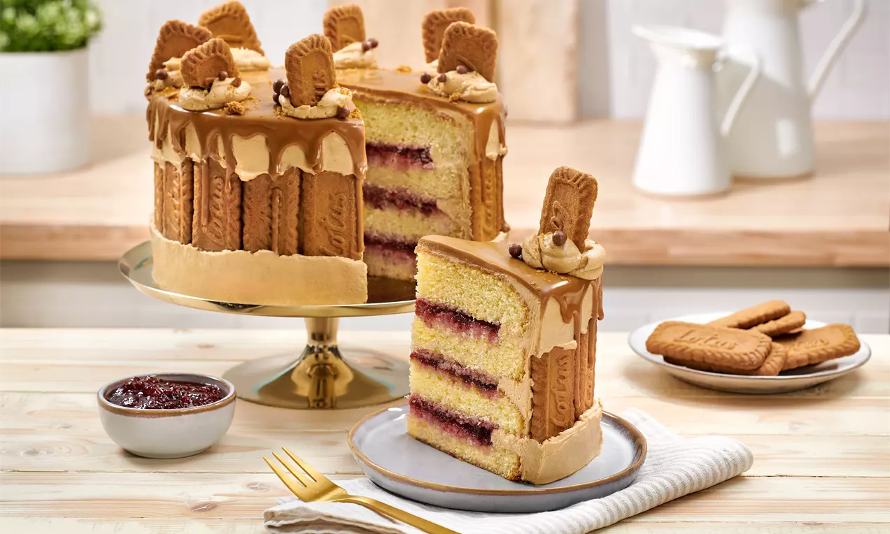 Fault-Line-Cake mit Biscoff-Keksen und karamellfarbener Creme, dreischichtig mit Marmelade gefüllt, ein Stück auf Teller mit Gabel angerichtet