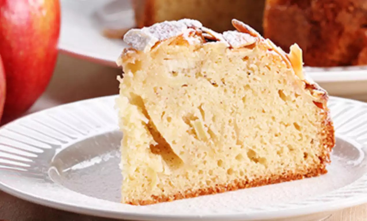 Slice of moist black tea cake with a golden-brown crust, soft crumb, almond flakes and powdered sugar on a white patterned plate