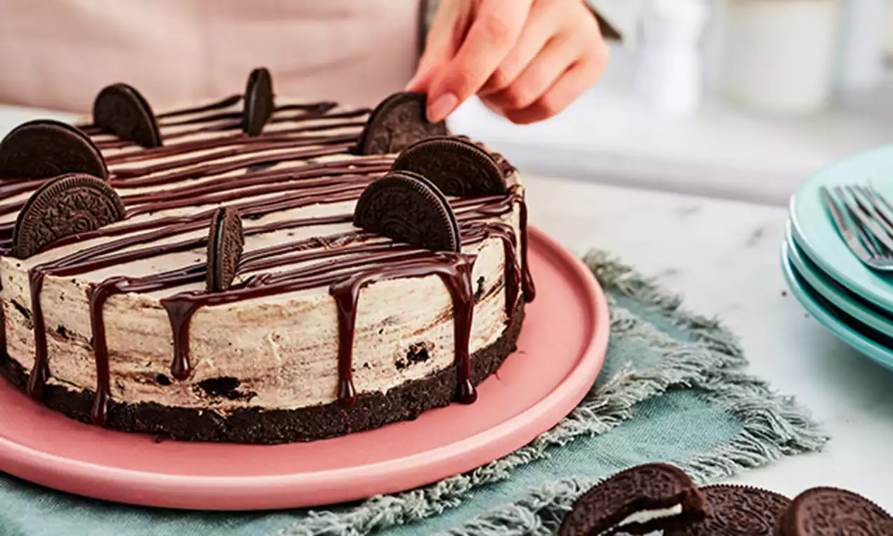 Oreo cheesecake with a speckled cream filling, dark biscuit base, drizzled chocolate and Oreo halves arranged on top on a pink plate