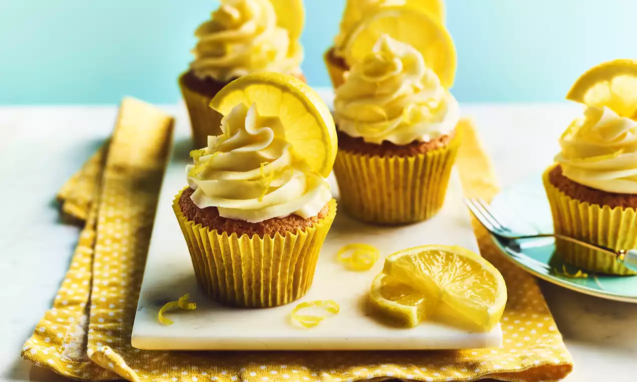 Golden cupcakes with creamy swirl frosting topped with vibrant lemon slices and zest arranged on a white rectangular platter