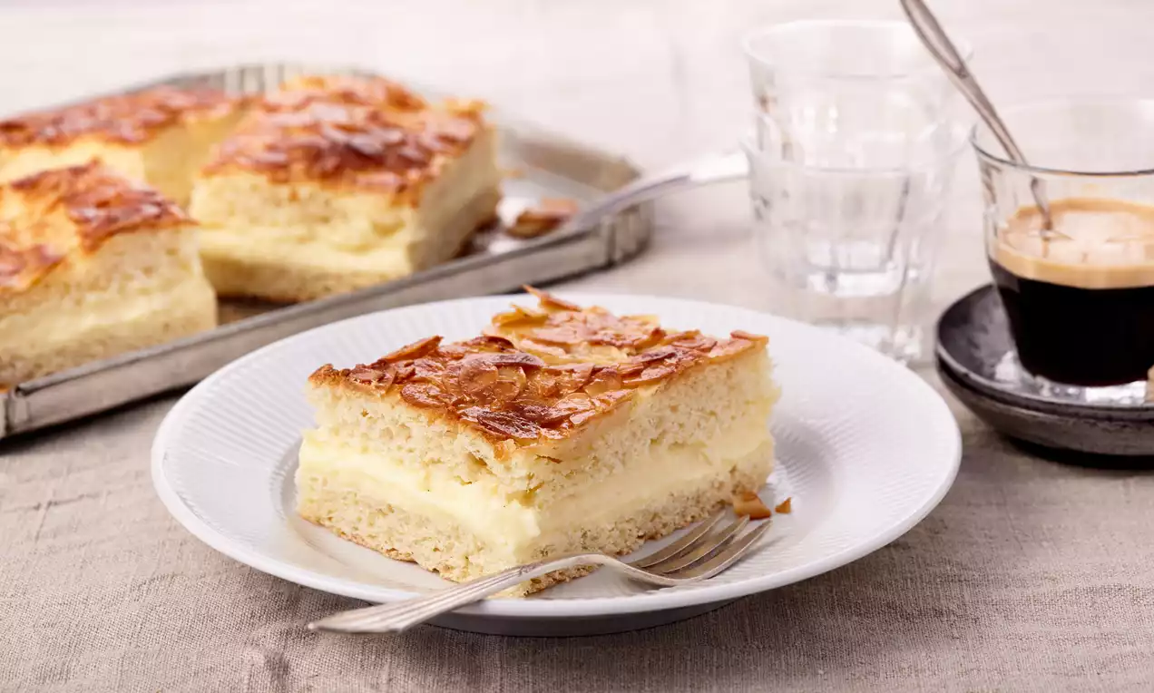 Bienenstich aufgeschnitten mit goldbraunem, knusprigem Mandelbelag, heller Vanillepudding-Füllung und luftigem Hefeteig