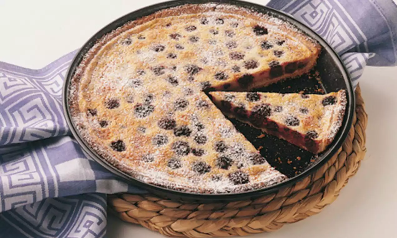 Goldbraune Brombeertarte mit saftigen, tiefvioletten Brombeeren und leichtem Puderzuckerschimmer auf geflochtener Unterlage und Stoffserviette
