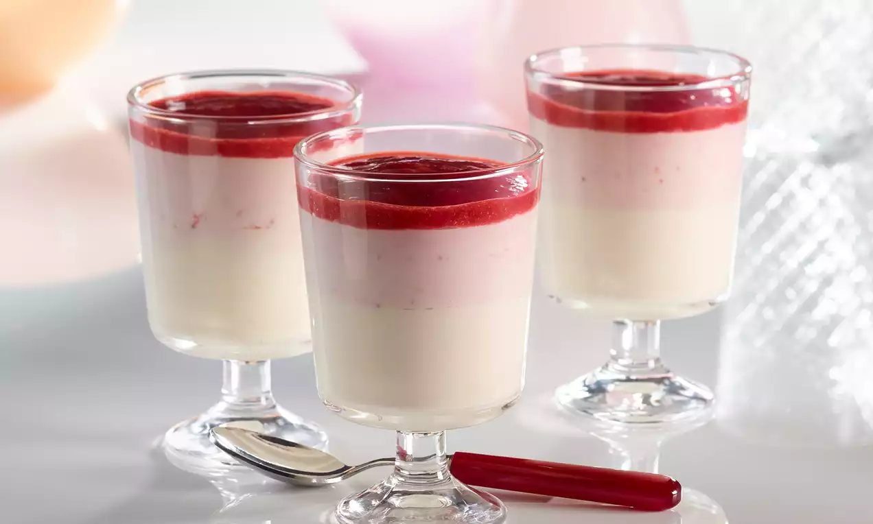 Geschichtete Creme aus weißer Schokolade, rosafarbener Erdbeerfüllung und rotem Fruchtspiegel serviert in klaren Dessertgläsern mit Löffel