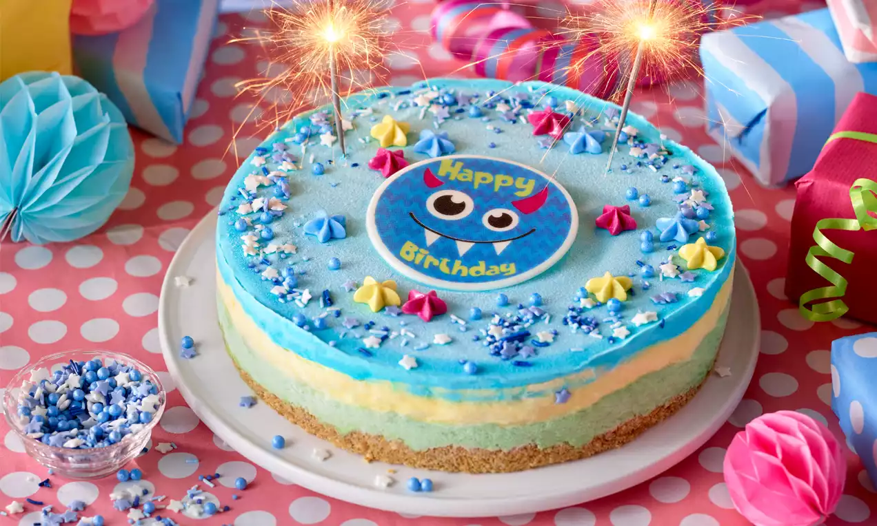Runde Torte mit blauem Guss, bunten Zuckerdekoren, einem Happy-Birthday-Emblem und Wunderkerzen auf weißer Tortenplatte