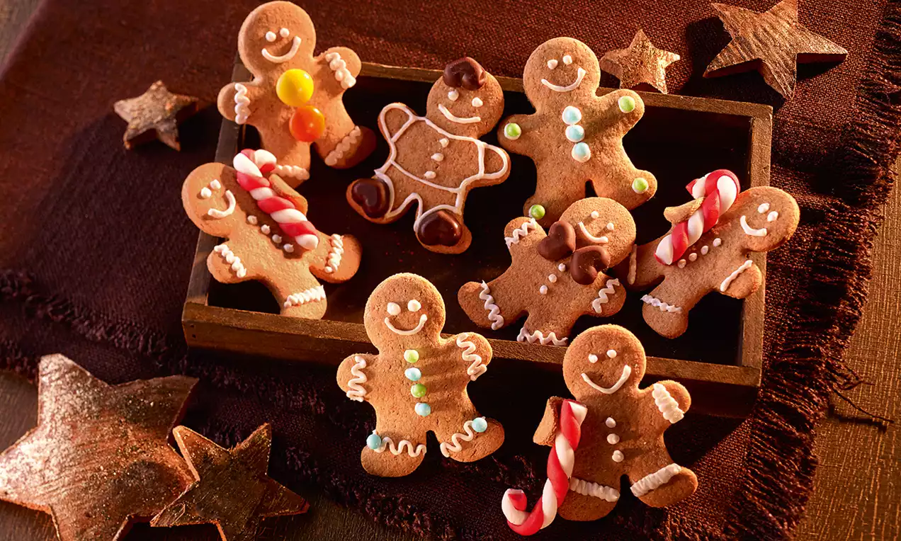 Zencefilli adam şeklinde kurabiyeler renkli şekerlemeler ve baston şeker detaylarıyla süslenmiş, ahşap bir kutuda yıldız detaylarla sunulmuş