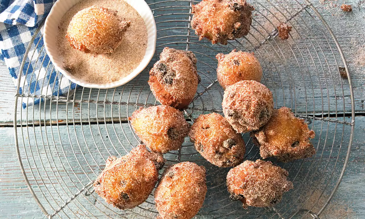 Zlatnosmeđi prženi kolačići nepravilnog oblika, posuti kristalnim šećerom na rešetki uz zdjelicu sa šećerom na drvenoj podlozi