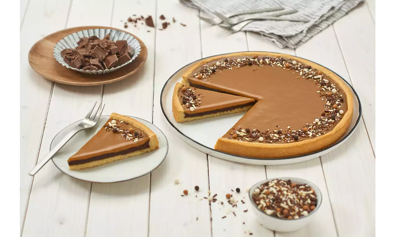 Salted Caramel Kuchen mit hellbrauner Karamellschicht und gehackten Nüssen am Rand, angeschnitten auf weißem Teller, daneben eine Kuchengabel