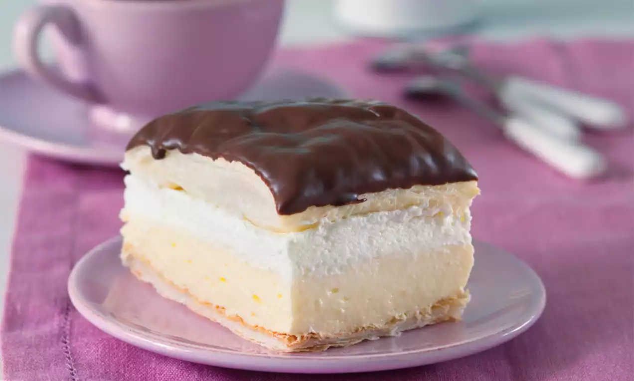 Krémový řez s vrstvou nadýchané šlehačky a světlého vanilkového krému na listovém těstě, pokrytý tmavou lesklou čokoládovou polevou