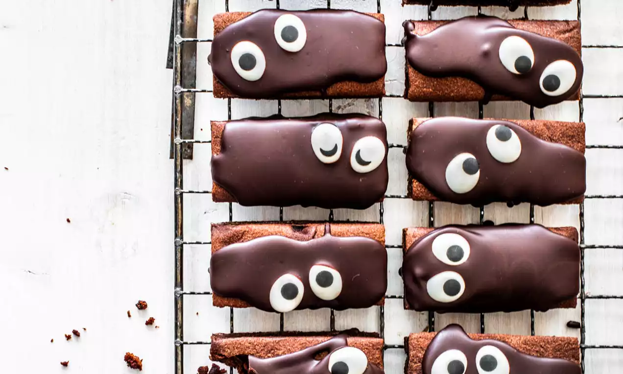 Donkerbruine rechthoekige brownies met glanzende chocoladeglazuur, versierd met witte oogjes, op een metalen koelrek