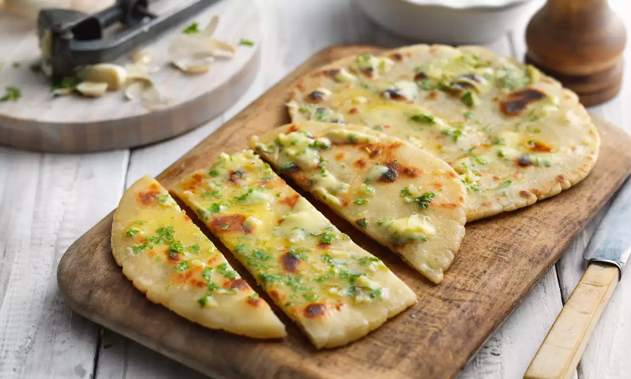 Golden flatbread with a soft, bubbled surface, scattered with melted garlic butter and parsley, served on a wooden board