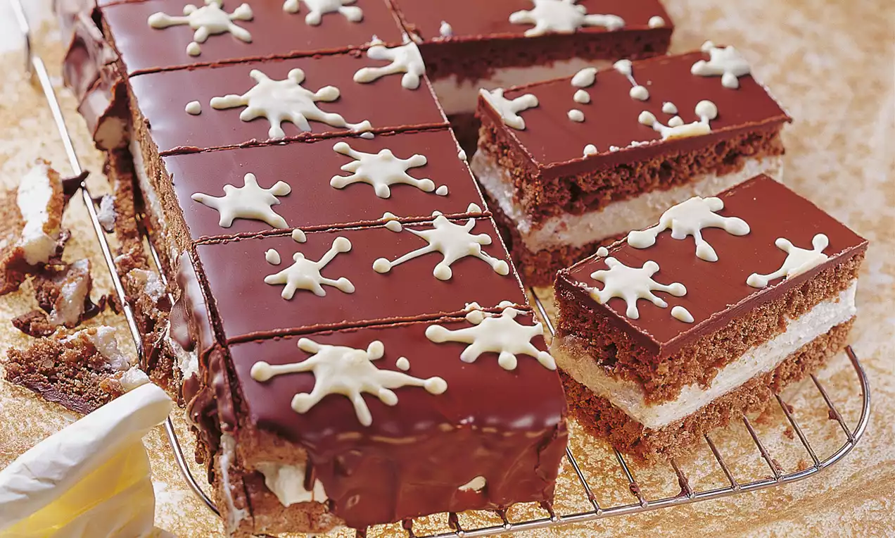 Rechteckige Milch-Kokos-Schnitten mit dunkler Schokoladenglasur und weißen Klecks-Verzierungen auf einem Kuchengitter angerichtet