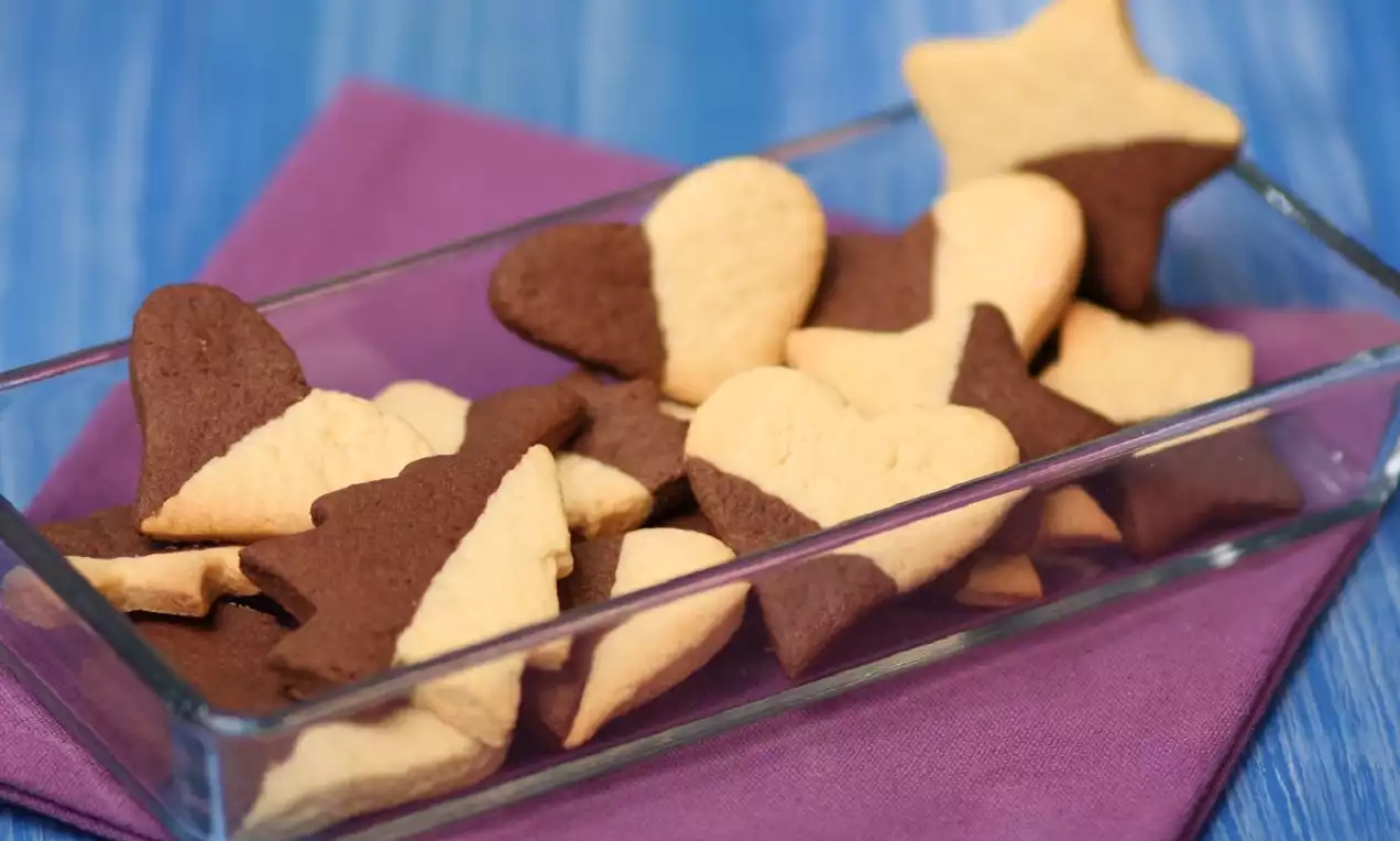 Kare cam tabakta sunulan, yarısı siyah yarısı beyaz kalp ve yıldız şekilli gevrek kurabiyeler mor örtü üzerinde düzenlenmiş