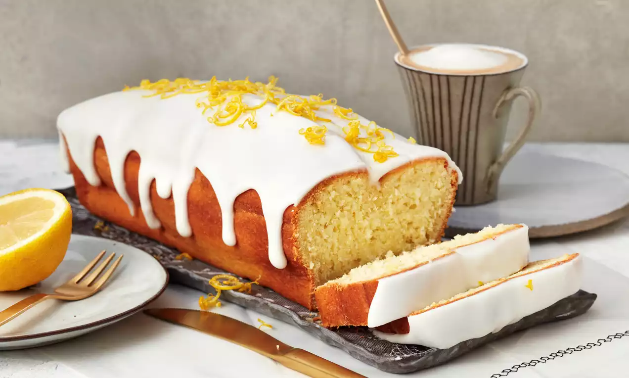 Zitronen-Joghurtkuchen mit glänzender Zitronenglasur, saftigen Kuchenstücken auf hellem Teller garniert mit Zitronenscheiben und Puderzucker