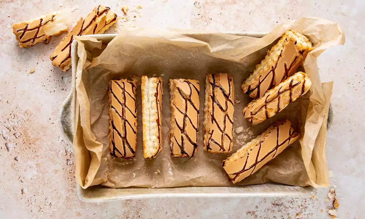 Sfogliatine dorate rettangolari con glassa caramello e decorazioni di cioccolato fondente su carta da forno dentro un vassoio