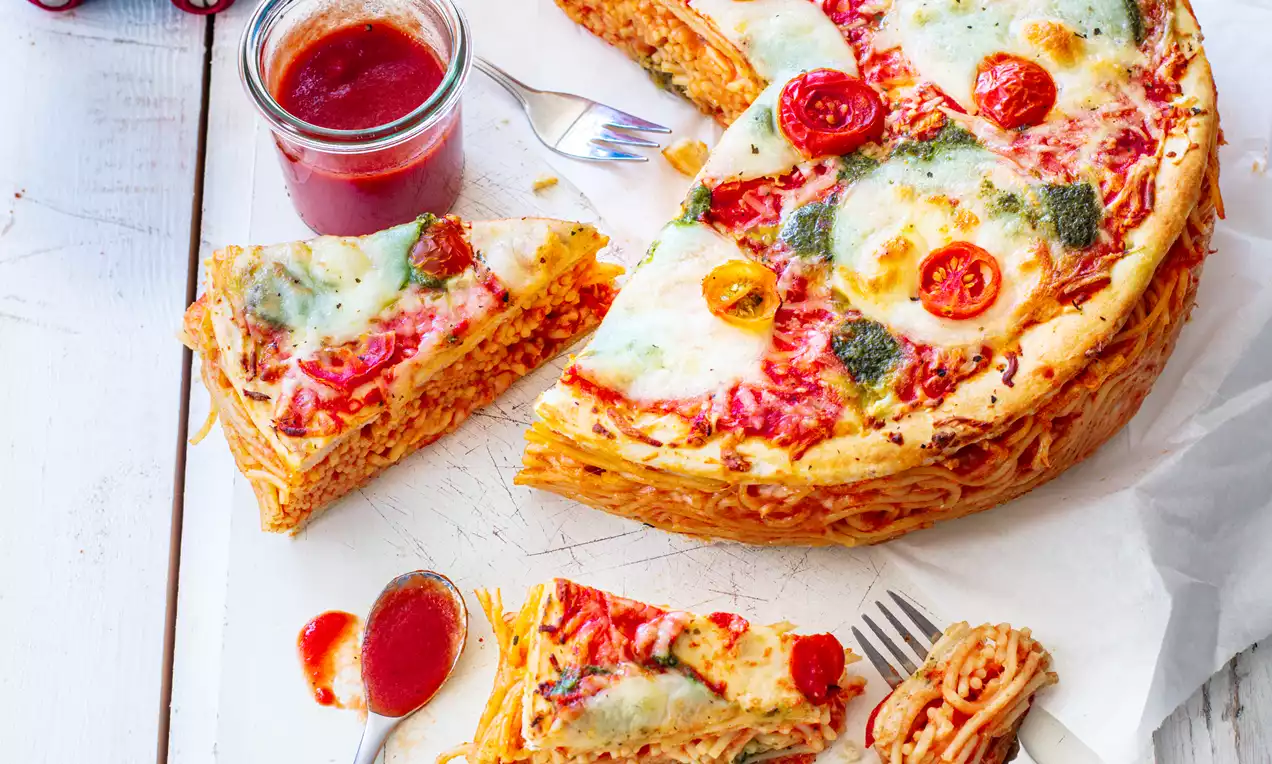 Ronde taart van goudbruine spaghetti met gesmolten kaas, rode tomatensaus, kerstomaten en kruiden op een wit houten oppervlak