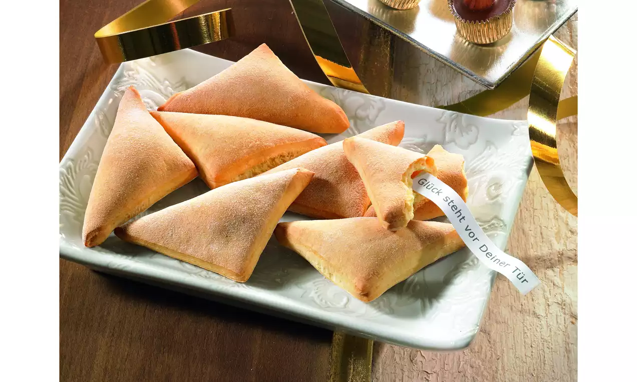 Goldbraune, dreieckige Glückskekse mit zarter Textur auf einer weißen, gemusterten Platte, eine Botschaft ragt aus einem Keks hervor