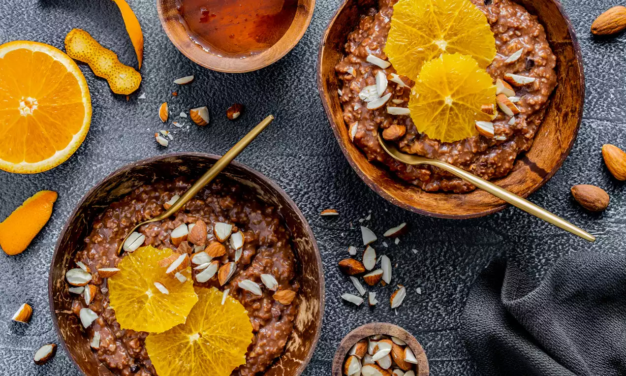 Schokoladen-Orangen-Porridge in braunen Schalen, dekoriert mit frischen Orange-Scheiben und gehackten Mandeln, auf dunklem Untergrund