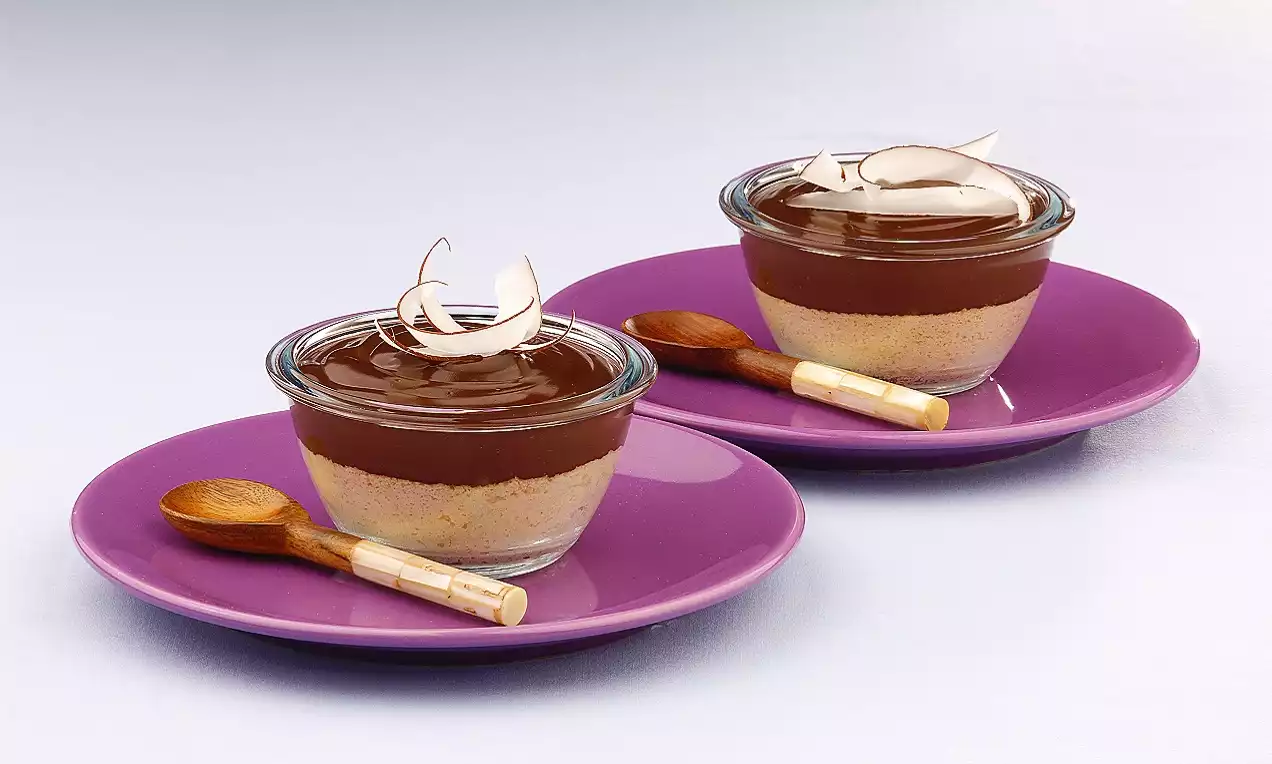 Cam kaselerde katmanlı görüntüsüyle kremsi bir dokuda çikolatalı ve bisküvi tabanı, hindistan cevizi dilimleriyle süslenmiş iki porsiyon