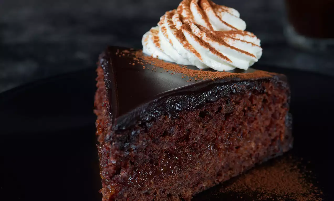 Čokoládový trojuholník s lesklou polevou, nadýchaný kakaový korpus a šľahačka so škoricovým práškom na tmavom tanieri