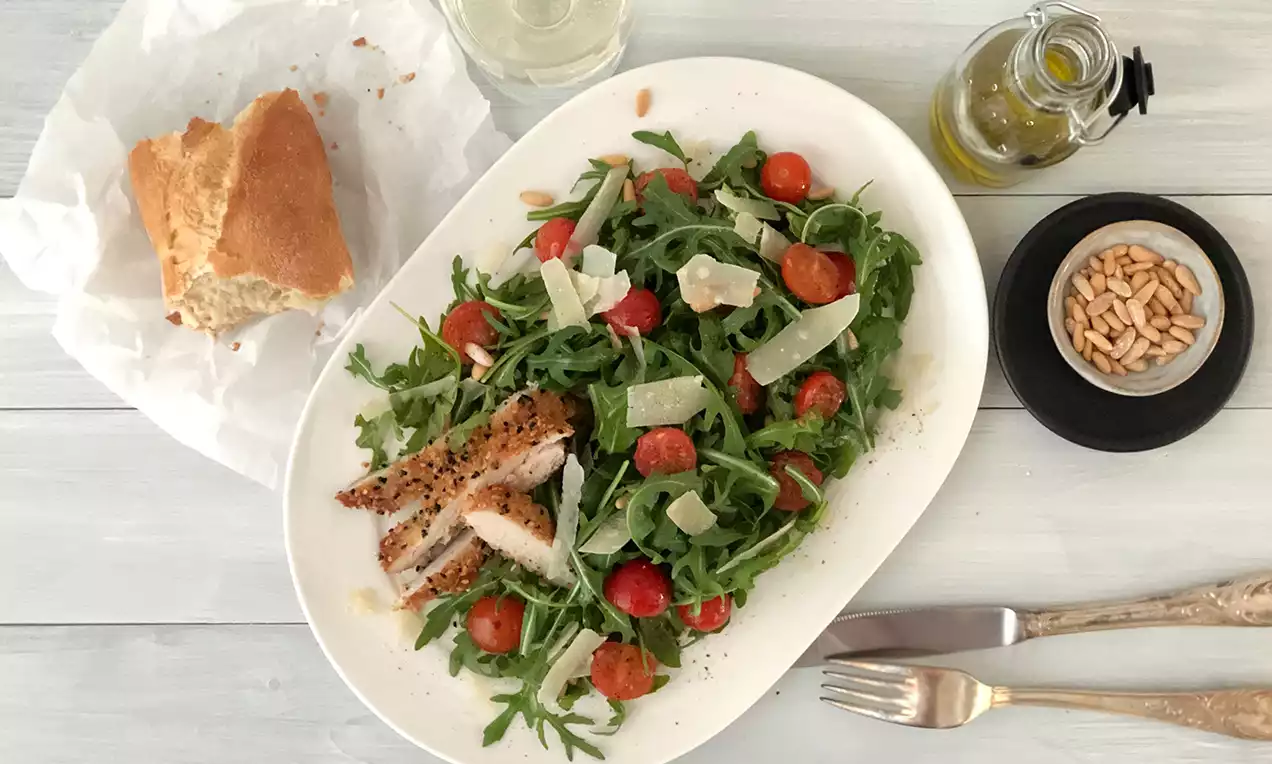 Rucolasalat mit gehobeltem Parmesan, grünen Blättern, roten Tomaten, gerösteten Pinienkernen und Honig-Balsamico-Dressing, schön angerichtet