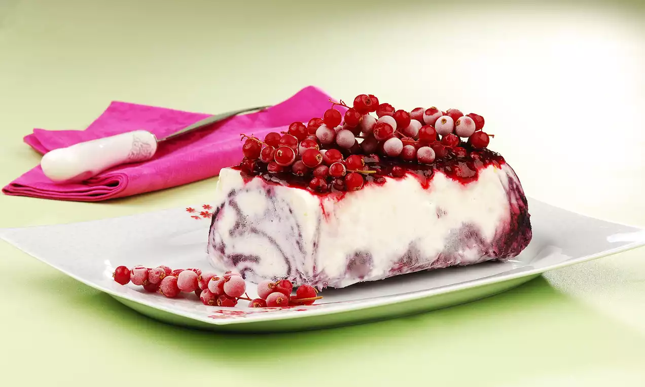 Beyaz tabakta sunulan, mor desenli kremamsı parfenin üzerinde orman meyveleri ve kırmızı sosla şık bir şekilde süslenmiş tatlı