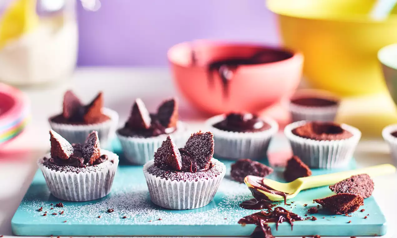Chocolate butterfly cupcakes in white paper cases on a turquoise board, topped with cocoa-dusted wings and surrounded by scattered crumbs