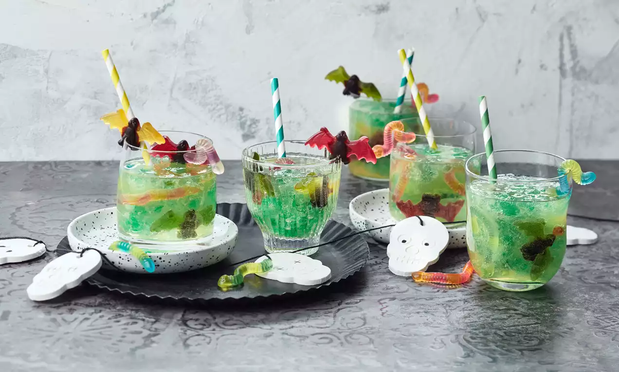 Halloween-Bowle mit leuchtend grüner Waldmeister-Götterspeise, Zitronenlimonade, Fruchtstücken und Zitronenscheiben im Glas
