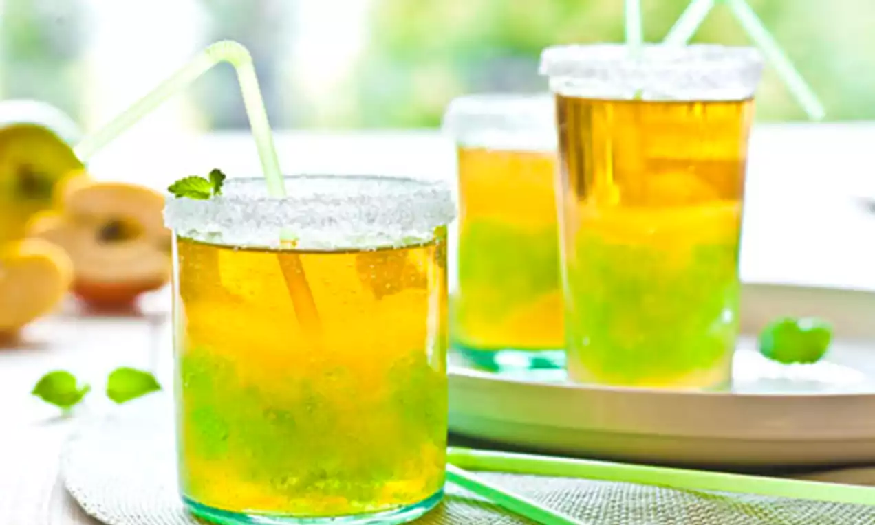 Szklanki z przejrzystym agrestowo-jabłkowym napojem w złocistozielonym odcieniu, musujące z owocowym miąższem, ozdobione cukrową krawędzią i listkiem mięty