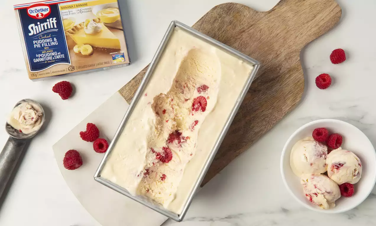 Glace onctueuse au tourbillon de framboises rouges et éclats de banane dorée dans un moule argenté sur une planche en bois avec des framboises