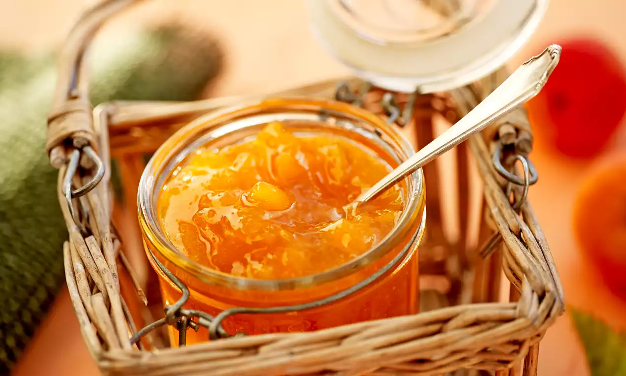 Glazen pot met glanzende oranje meloenconfituur, zachte textuur met stukjes, een lepel erin, geplaatst in een geweven mand