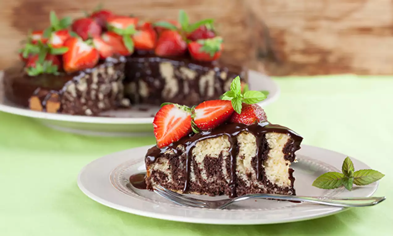 Slice of marble butter cake with swirls of chocolate and vanilla topped with glossy chocolate sauce, fresh strawberries, and mint leaves on a white plate