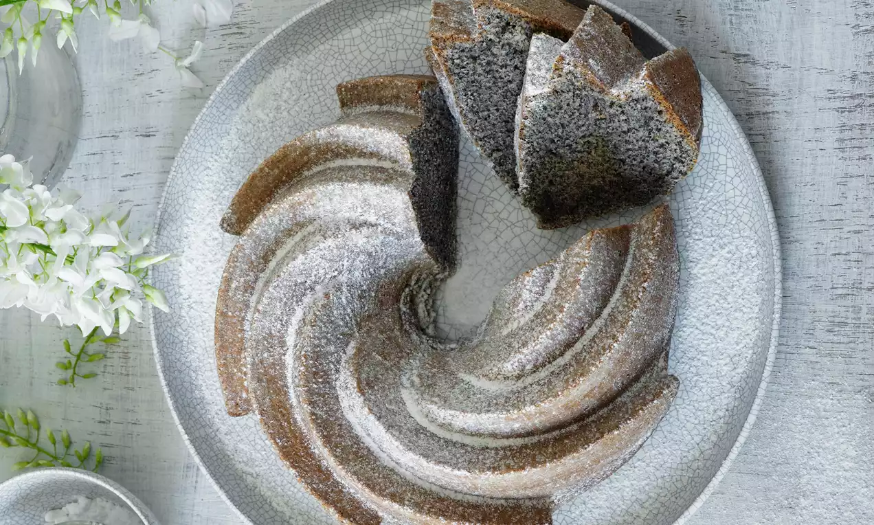 Maková bábovka tmavohnedej farby so špirálovým vzorom, jemne posypaná práškovým cukrom na svetlom keramickom tanieri