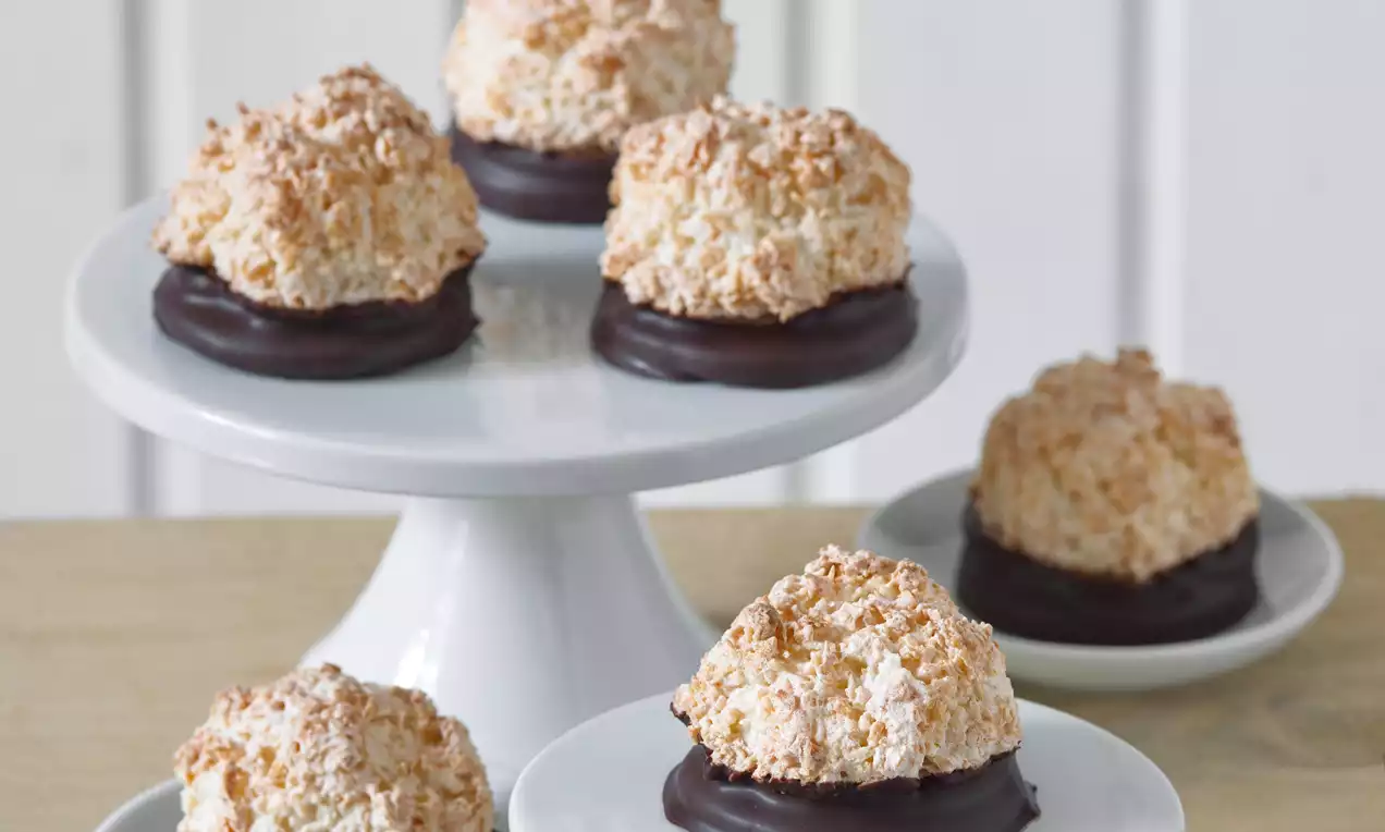 Zlatavohnědé kokosové hrudky s křupavou texturou na lesklém čokoládovém podkladu, elegantně naaranžované na bílém podnosu a talířku