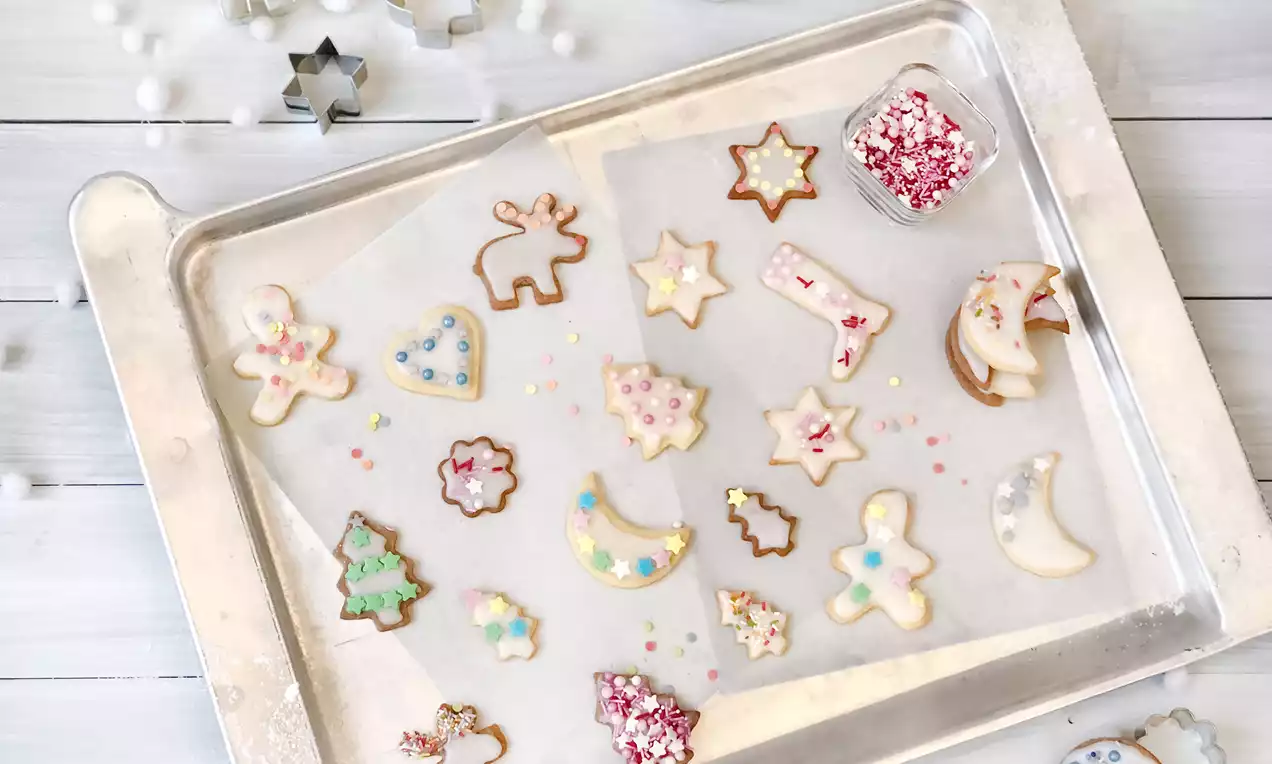 Ausstechplätzchen als Sterne und Figuren: goldbraun gebacken mit weißer, roter und grüner Glasur sowie bunten Streuseln auf Backpapier