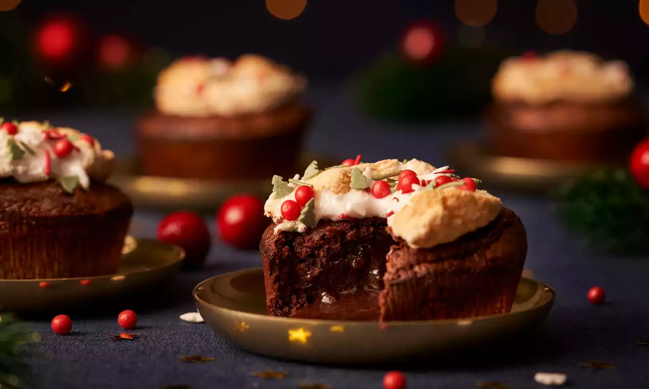 Donkerbruine chocolade-lava-cake met een zachte binnenkant, gegarneerd met witte crème, rode bessen en suikerdecoratie op een goudkleurig bord