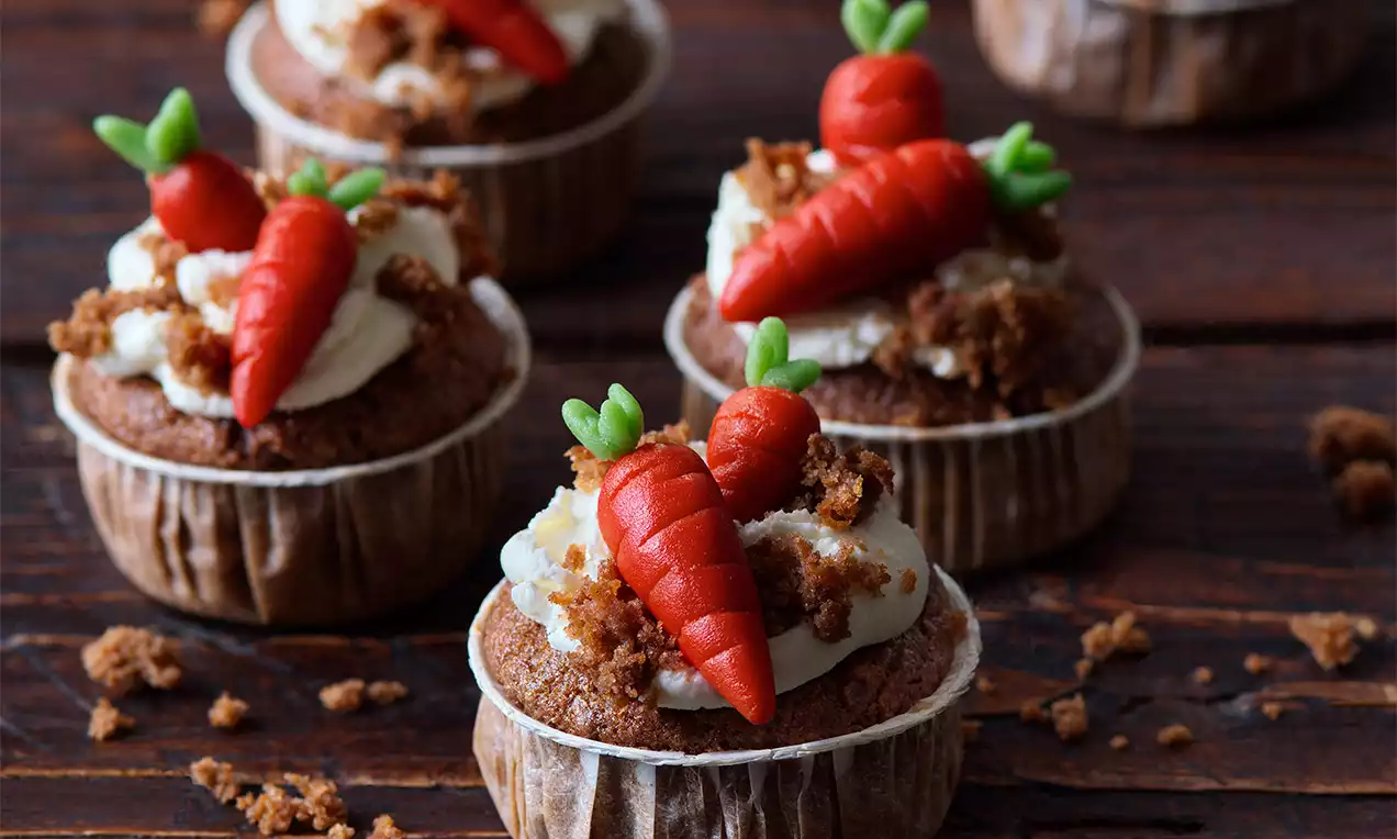 Mrkvové muffiny s jemným mascarpone krémom, ozdobené drobenkou a živými červenými marcipánovými mrkvičkami s lístkami