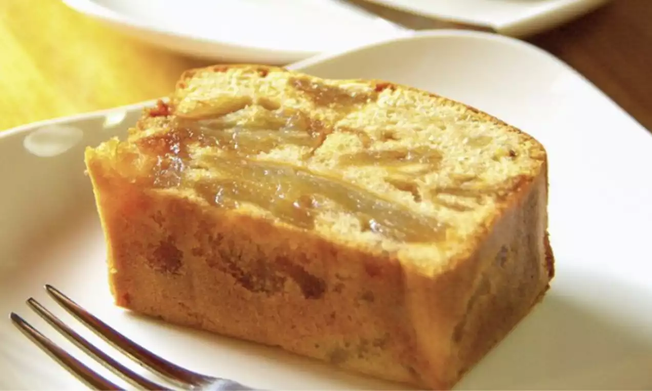 Golden rectangular slice of butter cake with chunks of chempedak fruit visible, served on a white plate beside a fork