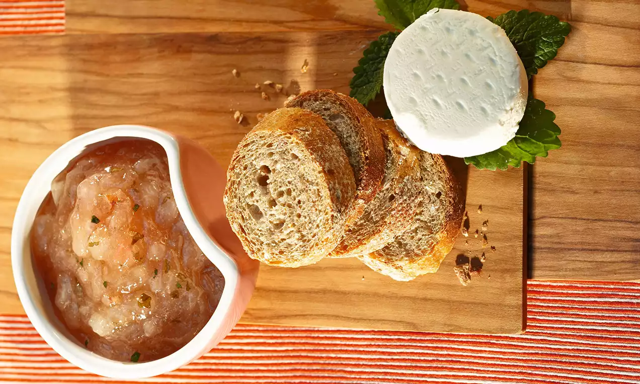 Svetlý hruškový džem s jemnou textúrou v bielej miske vedľa zlatistých krajcov chleba a kolieska syra na drevenej doske, ozdobené lístkami mäty