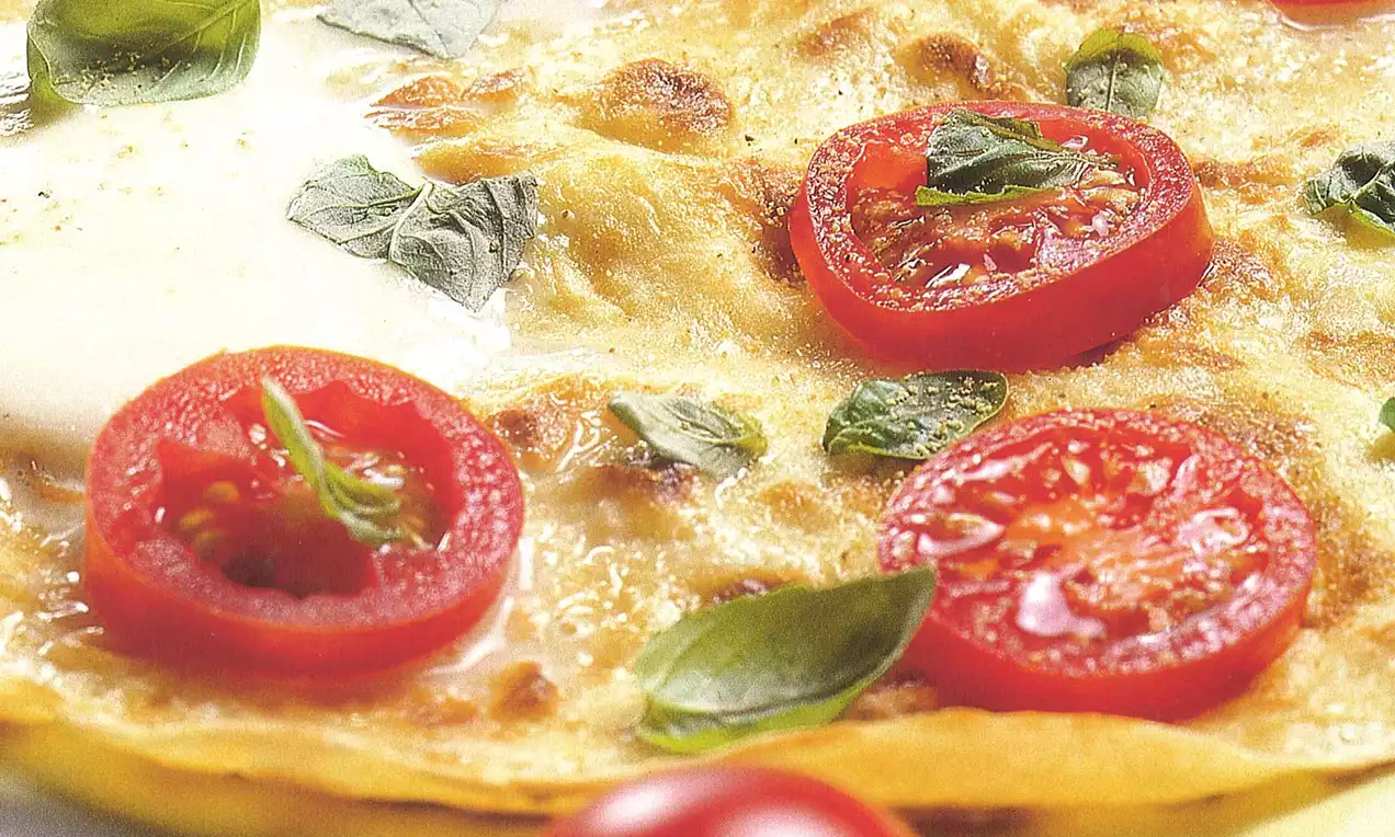 Crêpe dorée garnie de tranches de tomate rouge vif, mozzarella fondante et feuilles de basilic frais sur une assiette blanche