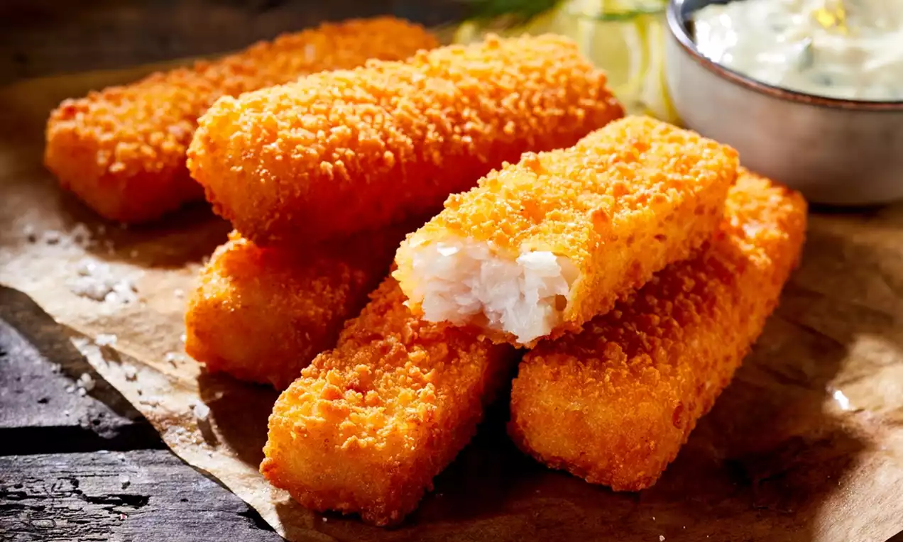 Golden breaded fish fingers with crisp texture, flaky white filling, arranged on parchment paper beside creamy tartar sauce and lemon slices