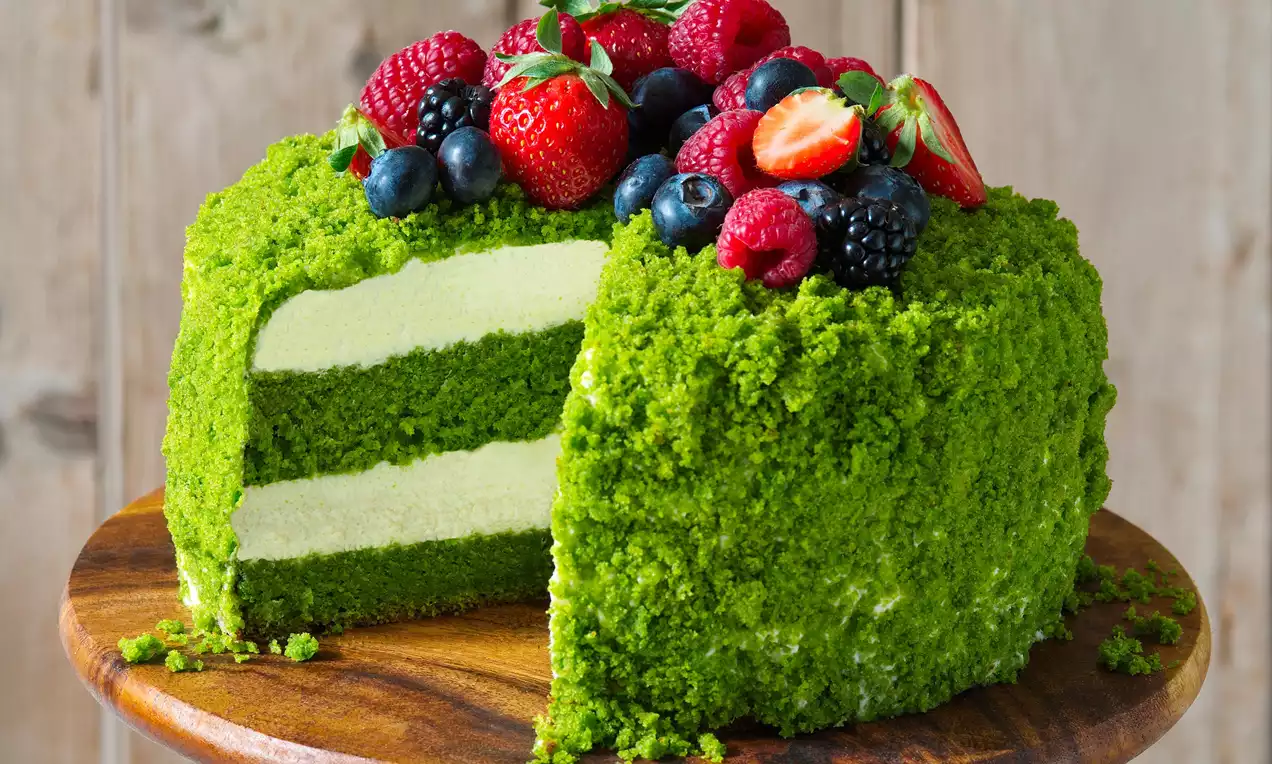 Mechový dort s jasne zeleným povrchom a dvoma vláčnymi vrstvami, ozdobený čerstvými jahodami, malinami a čučoriedkami na drevenom podnose
