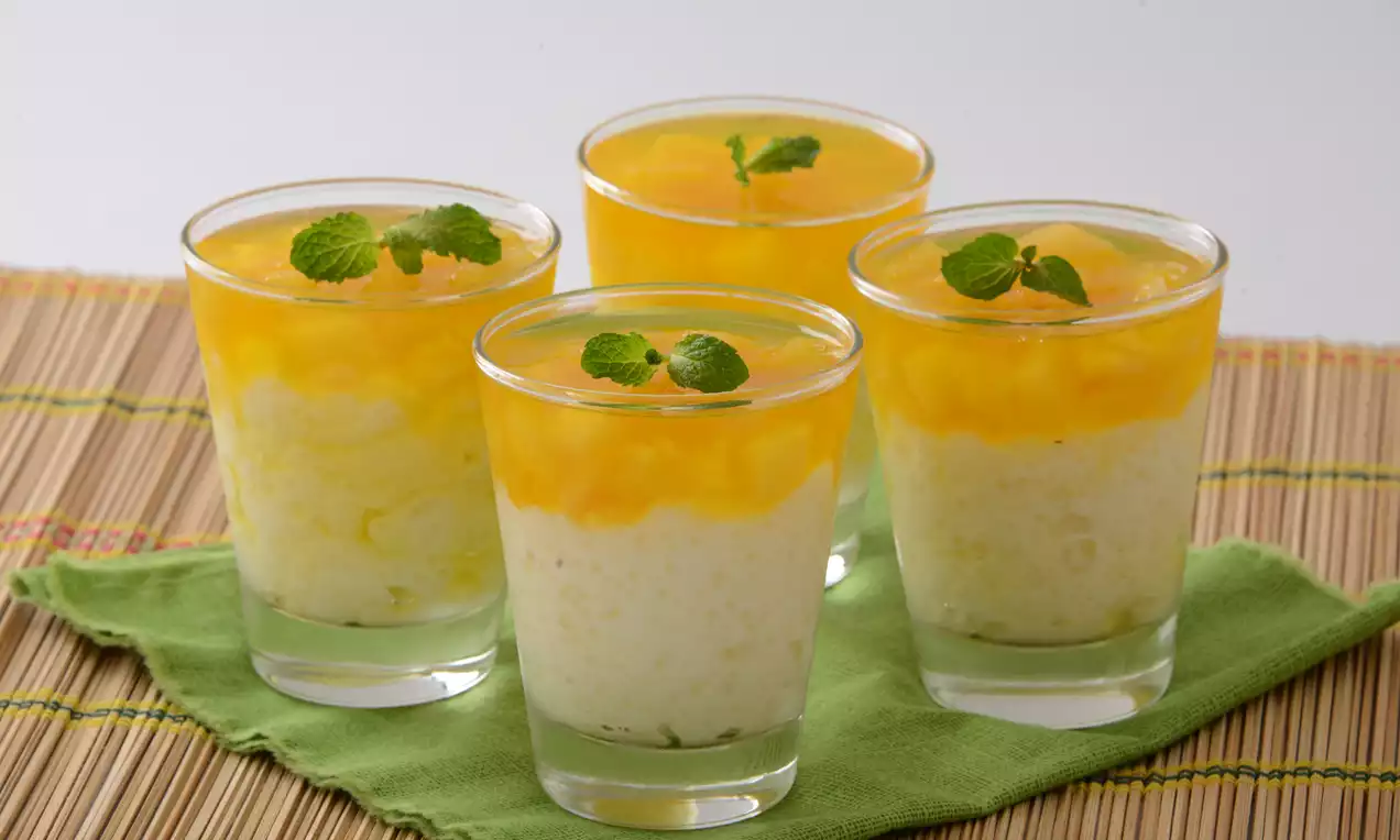 Sobremesas em copos transparentes com camadas de creme branco granulado e gelatina amarelo-viva, decoradas com folhas de hortelã