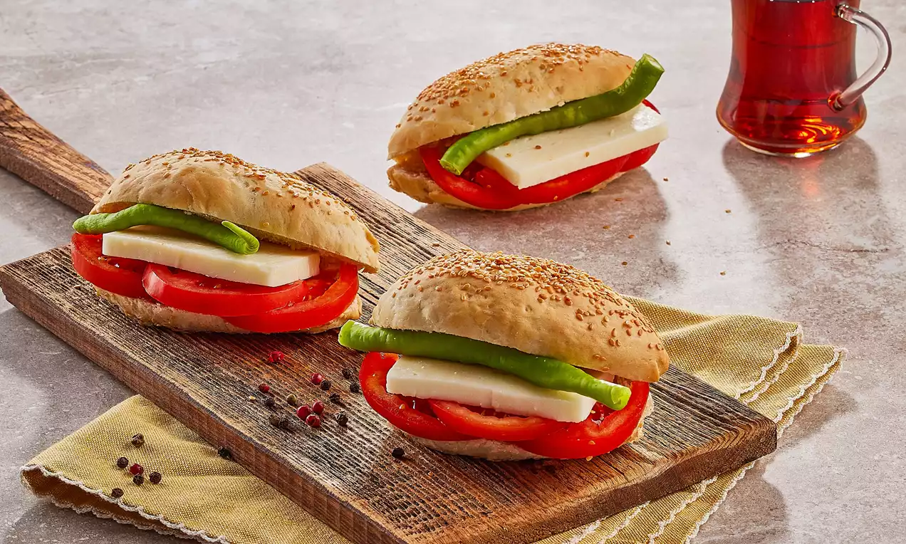 Susamlı çıtır kumru ekmeği içinde ince kesilmiş domates, beyaz peynir ve taze yeşil biberle ahşap bir sunum tahtası üzerinde